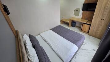 A bedroom with a bed, a bench, a small table, a mirror, and a wardrobe.