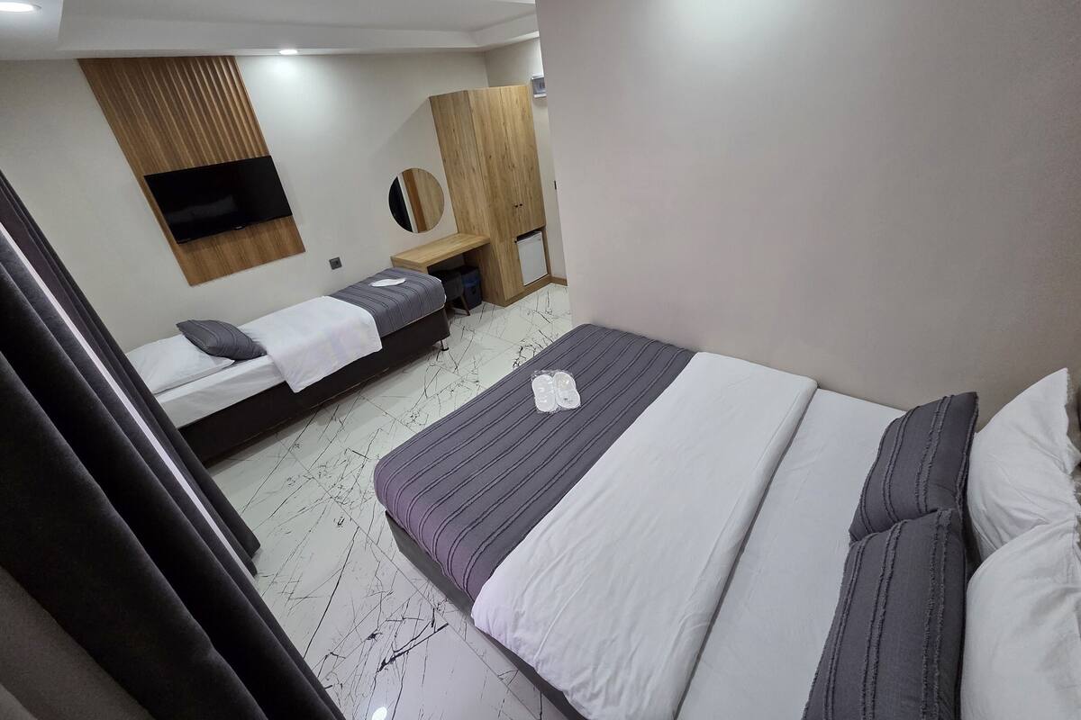 Een hotelkamer met een groot bed, een kleiner bed, een aan de muur bevestigde televisie, een houten kast en een bureau met een stoel.