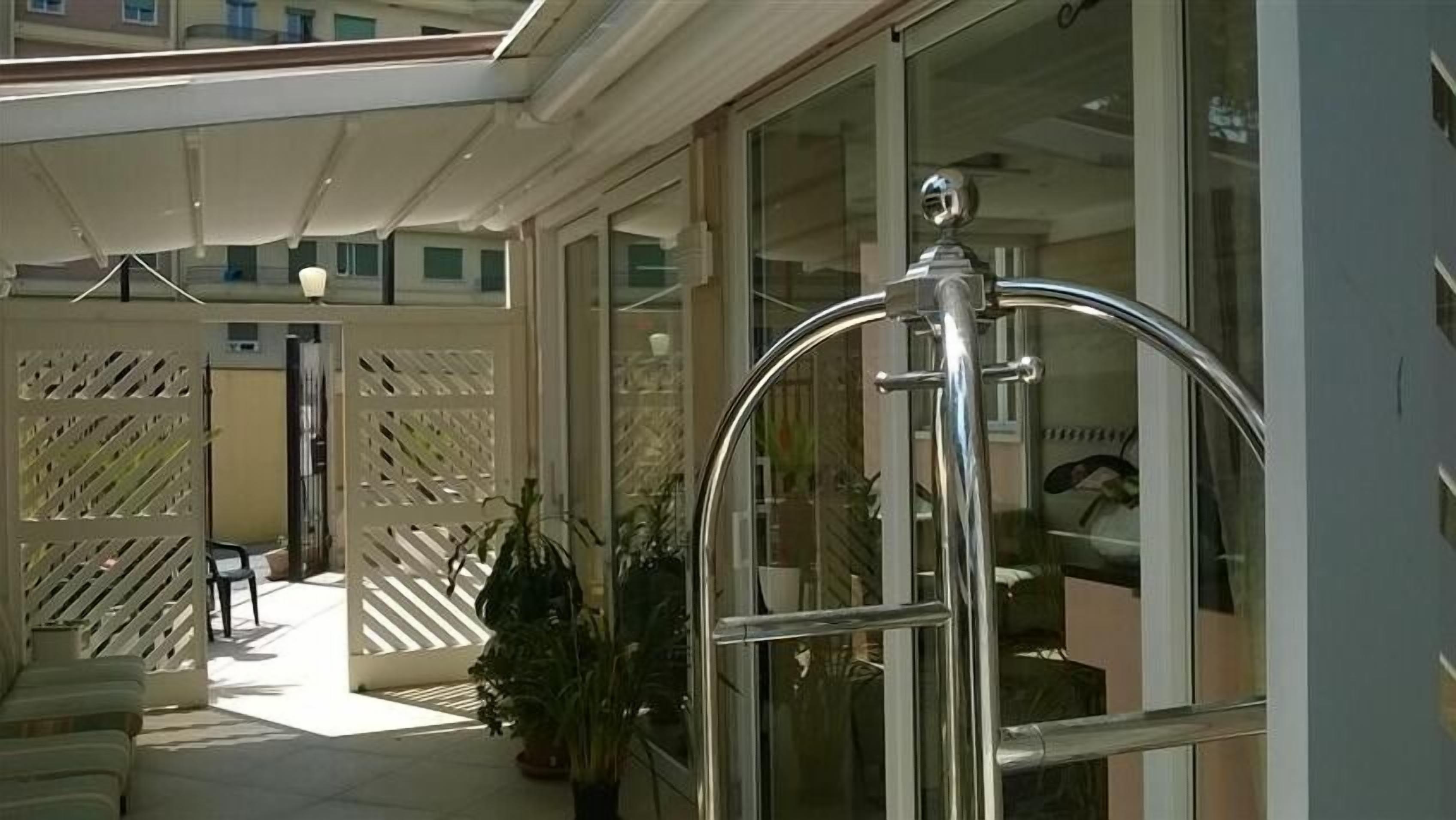A hotel entrance with a glass door, a metal gate, and a covered outdoor area with potted plants.