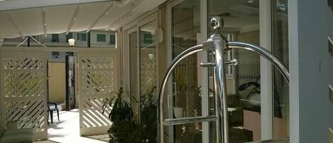 A hotel entrance with a glass door, a metal gate, and a covered outdoor area with potted plants.