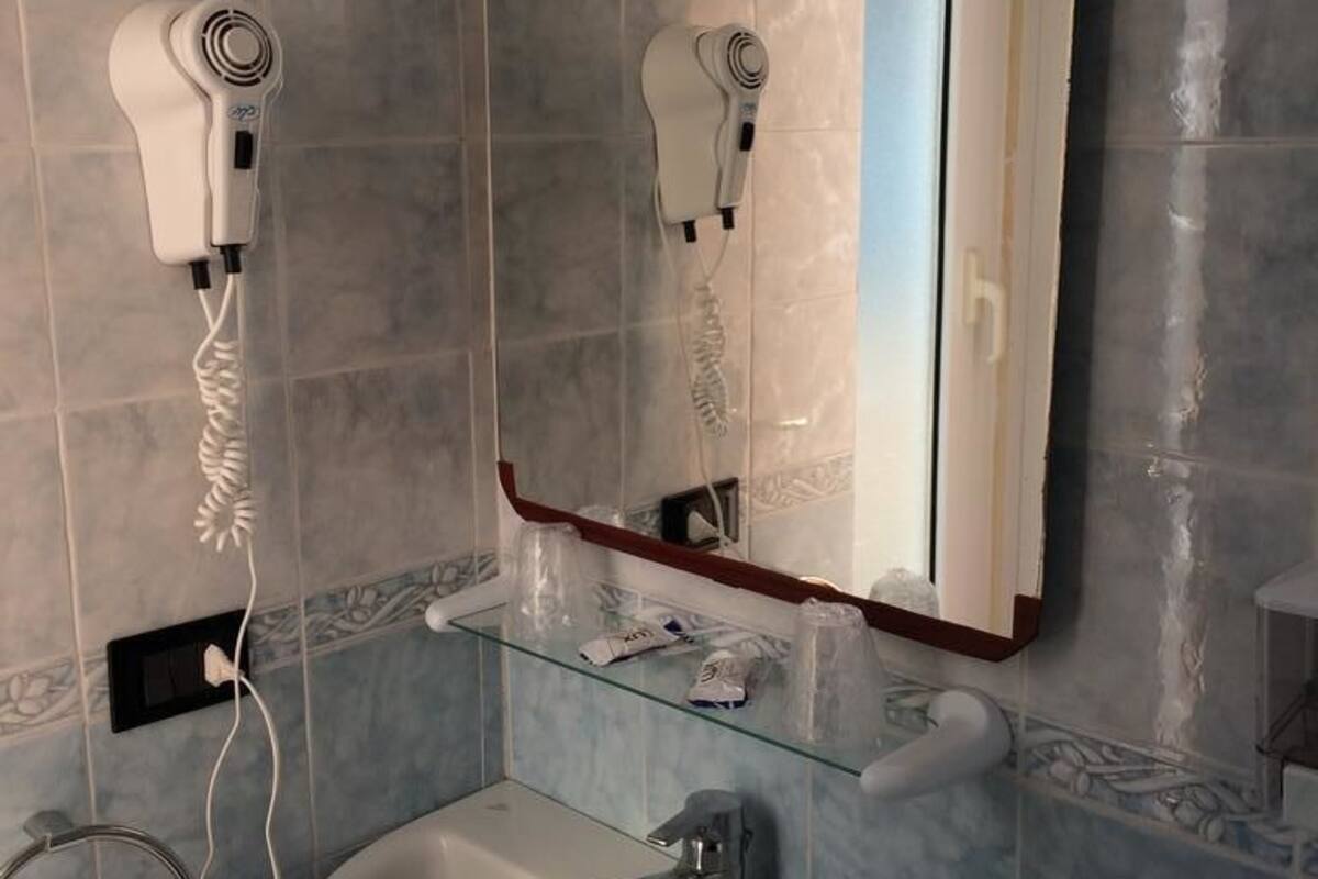 A bathroom with a sink, mirror, and two hair dryers mounted on the wall.