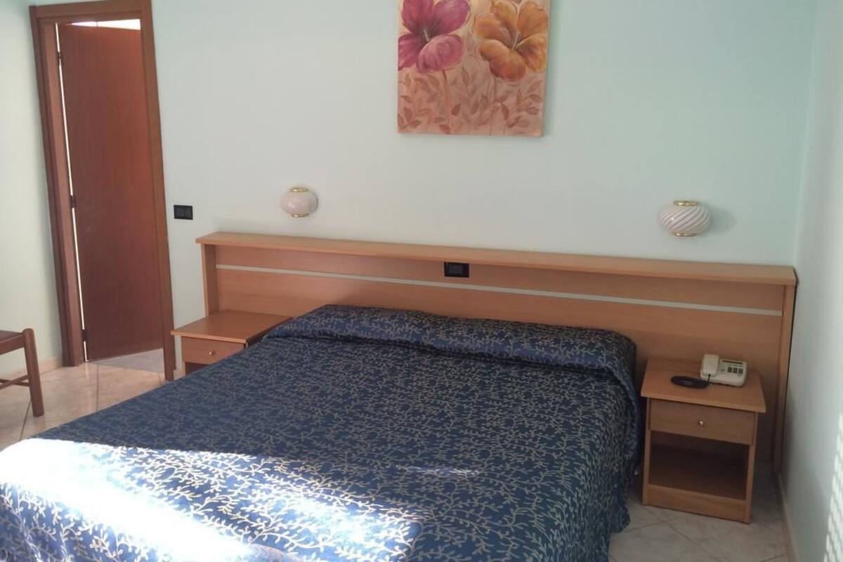A bedroom with a bed, a nightstand, a telephone, and a door.