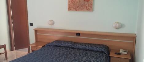 A bedroom with a bed, a nightstand, a telephone, and a door.