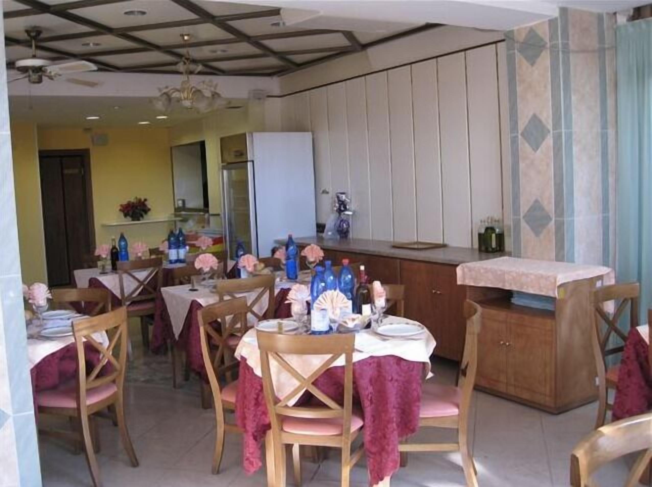Un coin repas avec des chaises et des tables en bois, un espace cuisine doté d’un comptoir et un ventilateur de plafond.