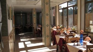 Un comedor con mesas y sillas, ventanas amplias y piso de baldosas.