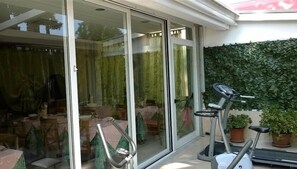 Un patio moderno con puerta de vidrio que da a un área de comedor, una bicicleta estática y una planta en maceta.