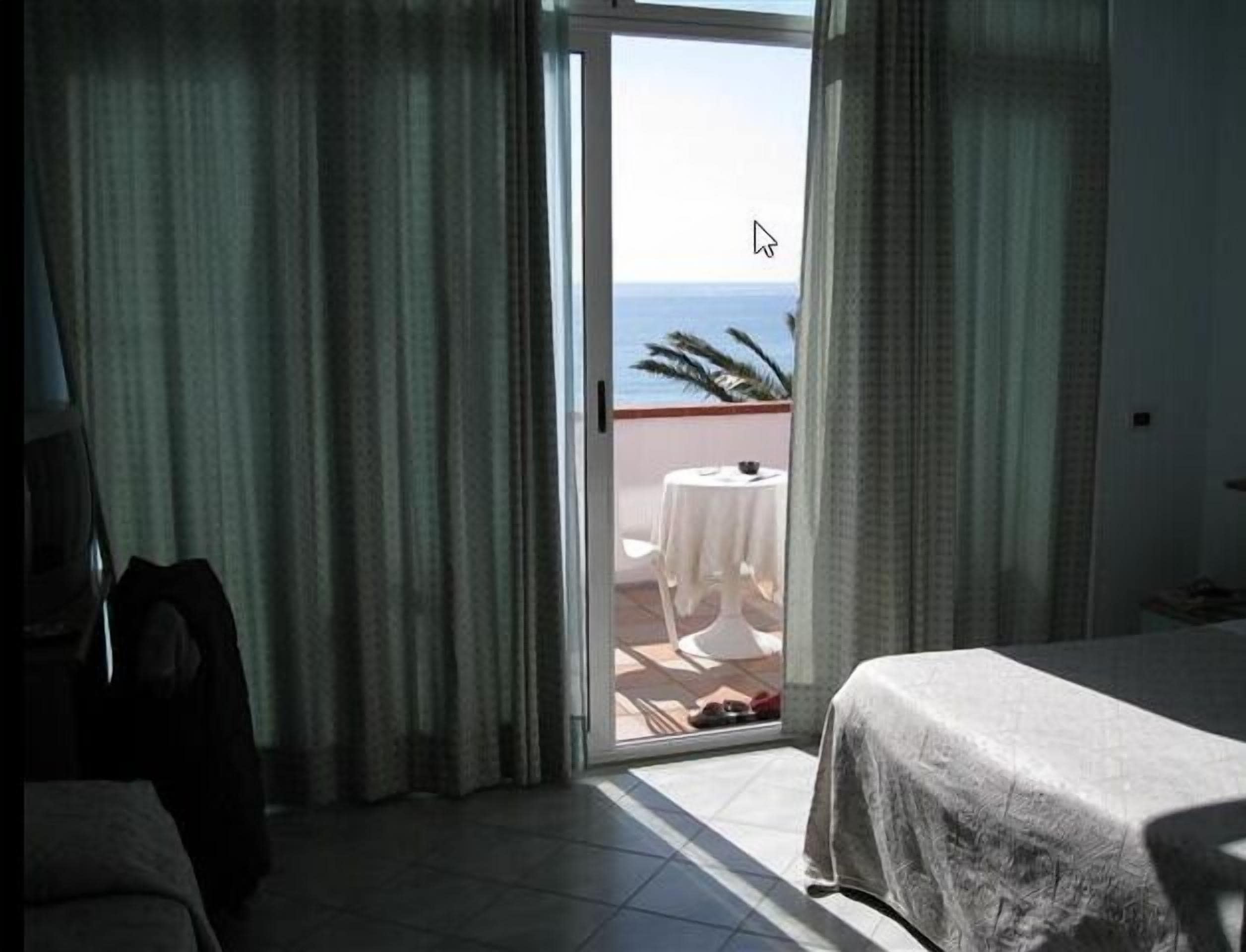 Una habitació d'hotel amb un llit, una cadira, una taula amb estovell blanc i vistes a l'oceà a través d'una porta corredissa.