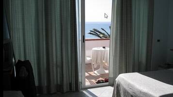 A hotel room with a bed, a chair, a table with a white tablecloth, and a view of the ocean through a sliding door.