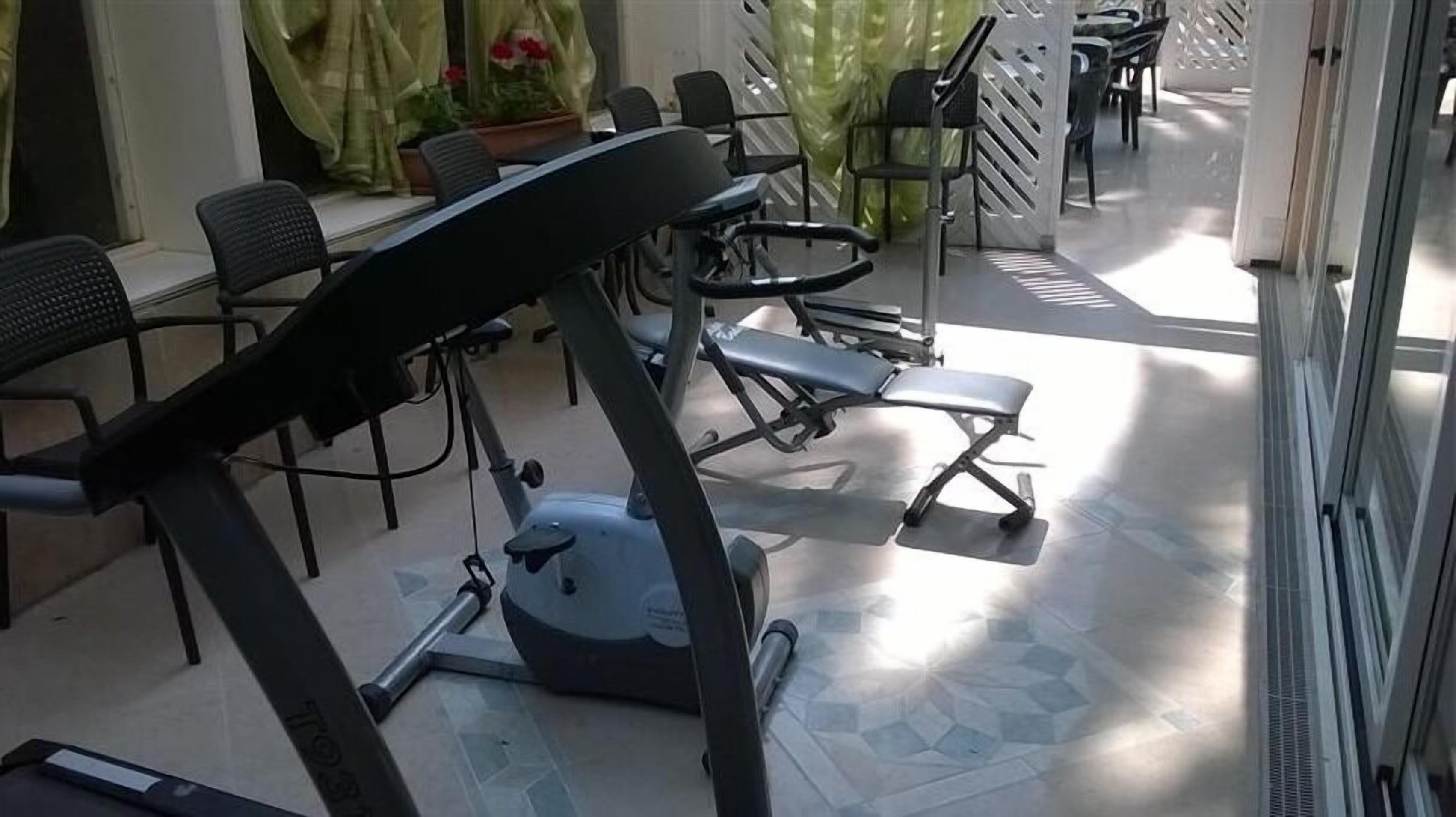 Un gimnasio con equipo de ejercicio, incluyendo cintas de correr y bicicletas estáticas, dispuesto en un espacio amplio con sillas y mesas.
