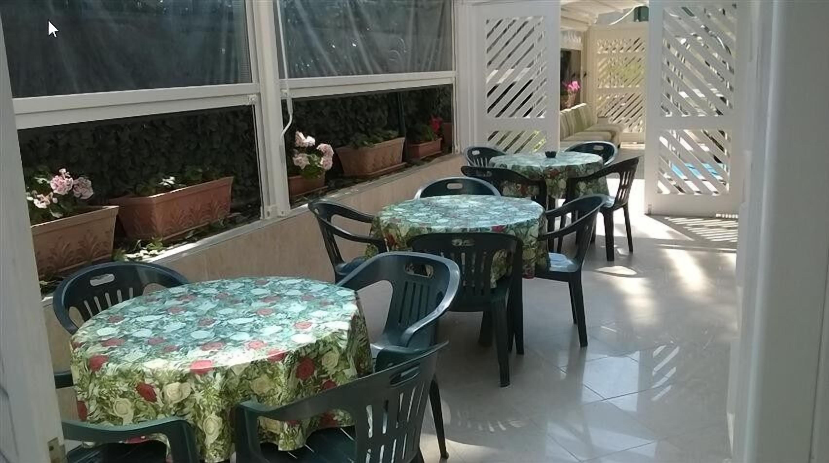 Un'area patio con tavoli e sedie rotonde, piante in vaso e una vista attraverso una finestra.