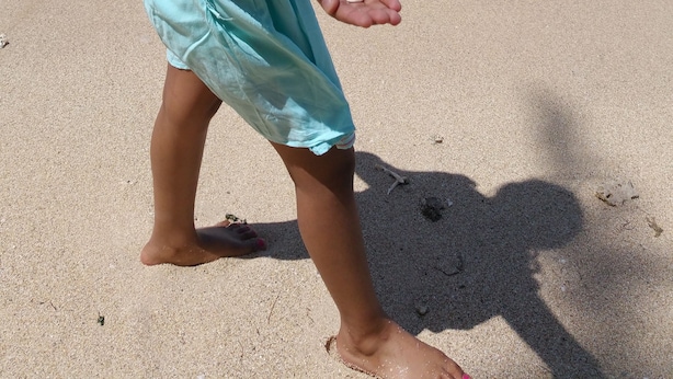 A child playing on a sandy beach with clear blue water and waves in the background. - Ariambello Vacation (Riambel)