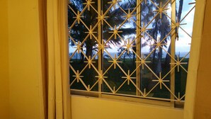A window with a yellow grid pattern, a view of palm trees, and a body of water in the background. - Ariambello Vacation (Riambel)
