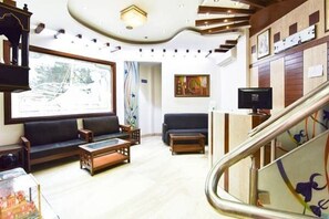 Un hall espacioso con una escalera moderna, un área de descanso con sofás y una mesa de centro, y obras de arte en las paredes.