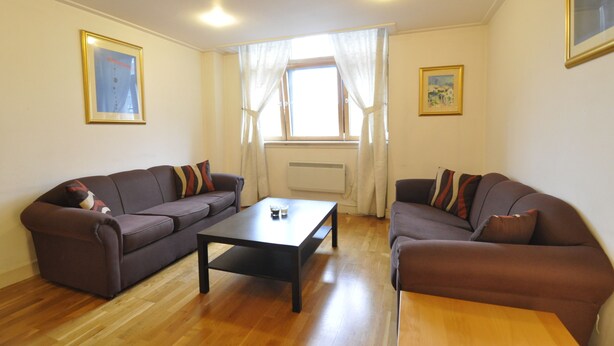 A living room with two brown sofas, a black coffee table, and a window with white curtains. - CityGate Old Street (London)
