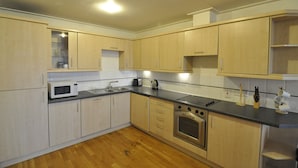 A modern kitchen with wooden cabinets, a microwave, a stove, and a sink. - CityGate Old Street (London)
