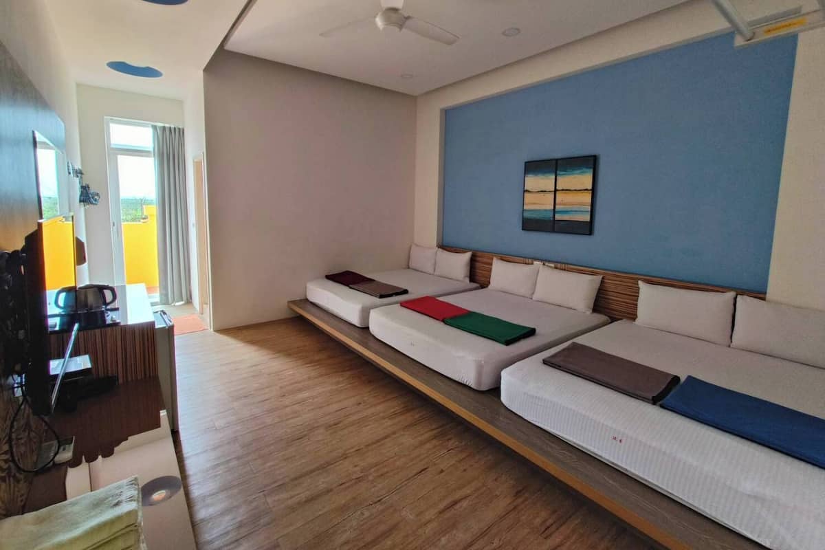 A hotel room with a long sofa bed, a ceiling fan, a painting on the wall, and a wooden floor.