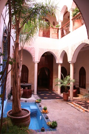 Ein Innenhof mit Pool, Topfpflanzen und einem Holztisch.