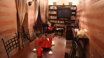 A cozy dining area with a wooden table, chairs, candles, and a bookshelf with books and a television.