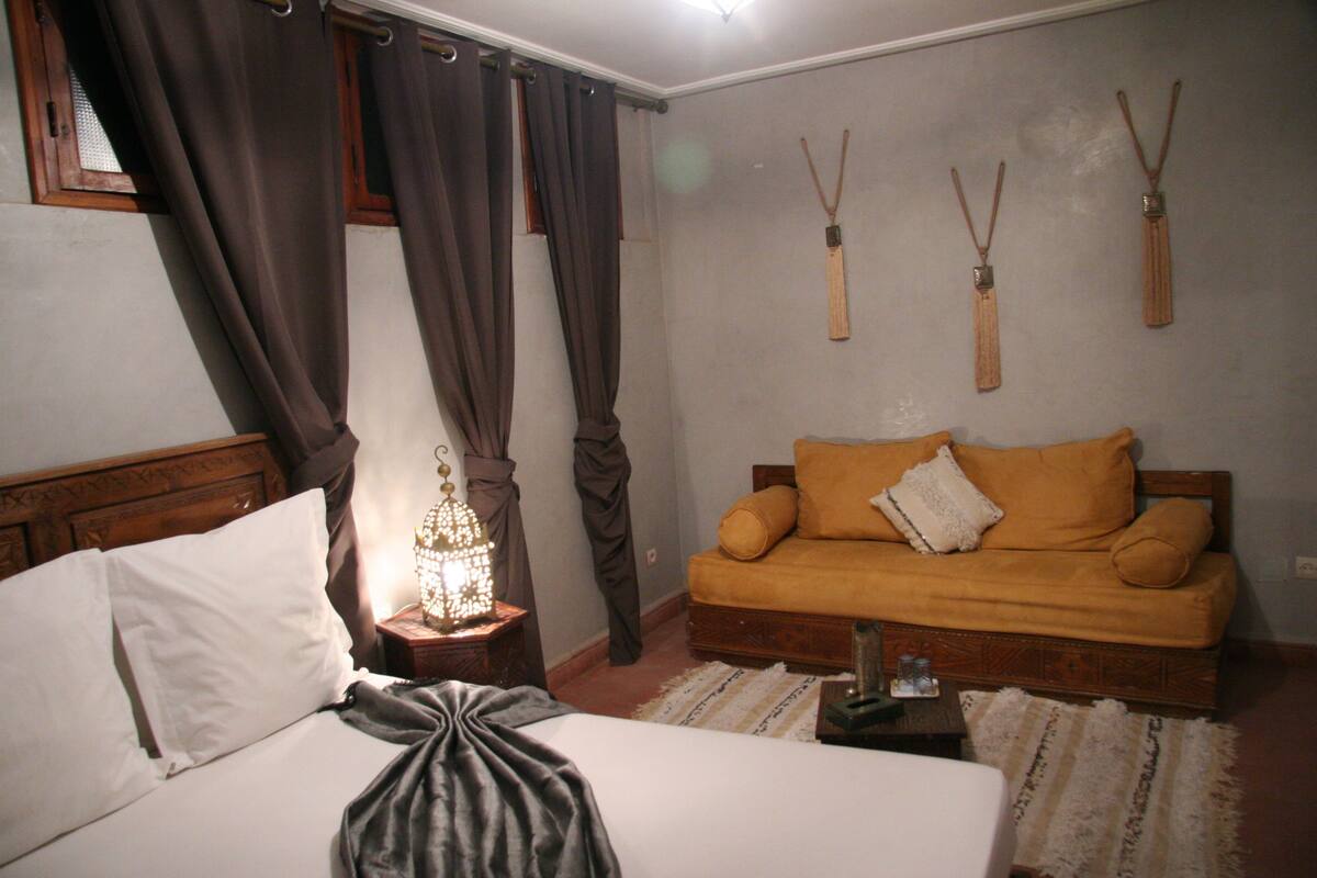 A bedroom with a bed, a nightstand with a lamp, a sofa, and wall-mounted tassels.