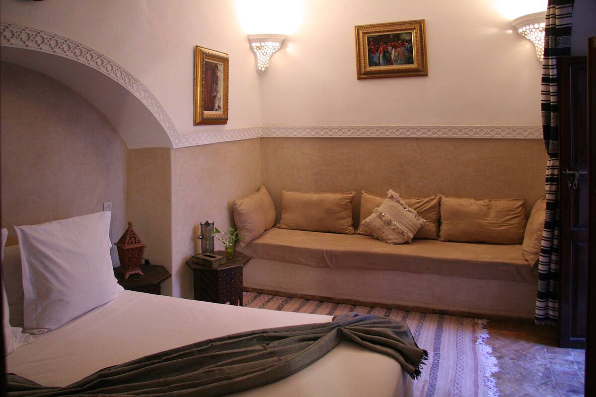 A bedroom with a bed, a sofa, a lamp, and a painting on the wall.