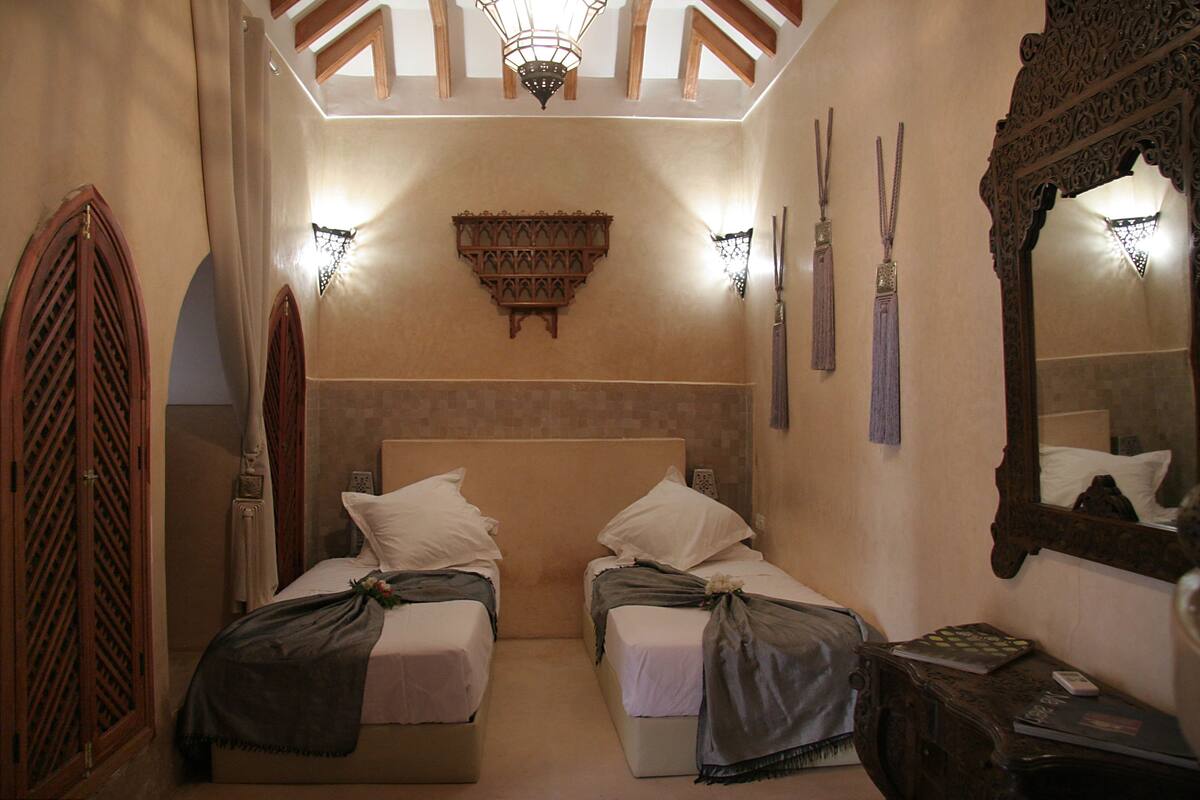 A room with two beds, a wooden headboard, a wall-mounted shelf, and a mirror.