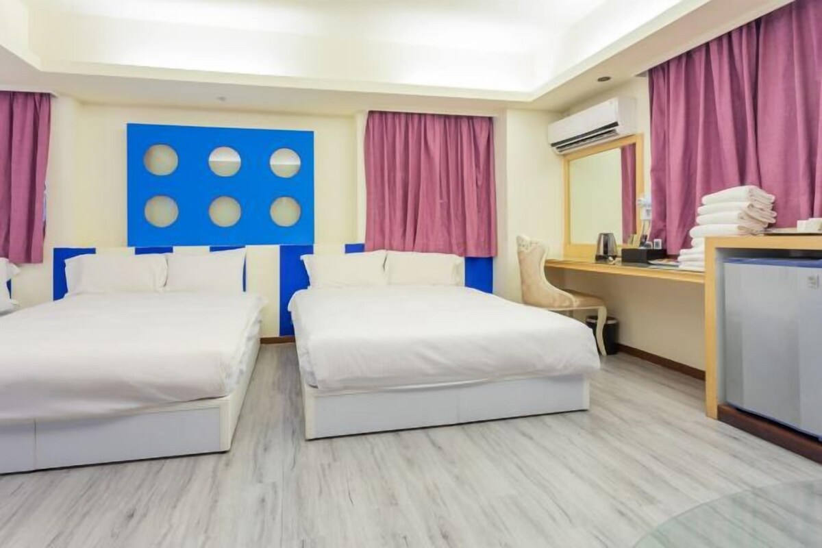 A hotel room with two beds, a desk, a chair, a mirror, and a wardrobe.