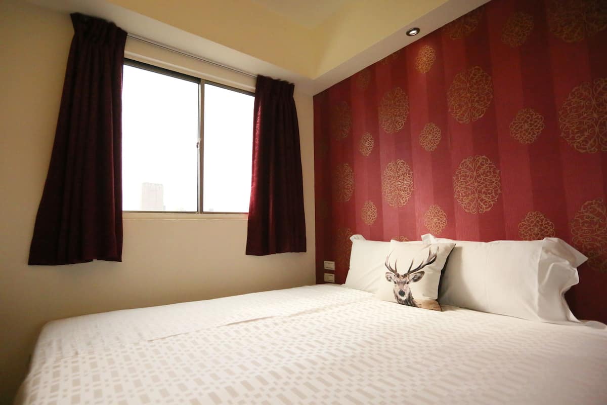 Ein Hotelzimmer mit Bett, einem Fenster mit Vorhängen und einer roten Wand mit Muster.