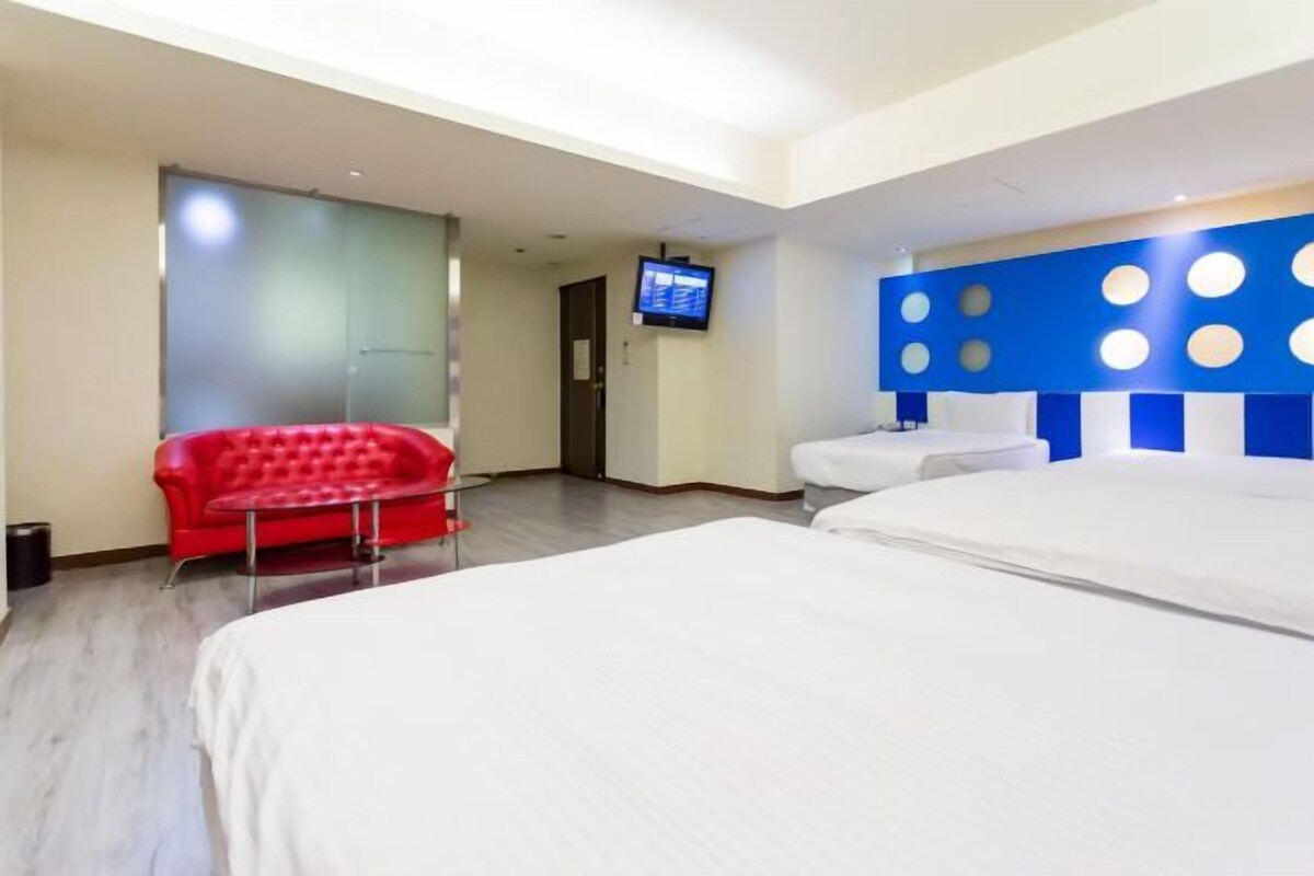 A hotel room with a bed, a red chair, a TV, and a wall with circular patterns.