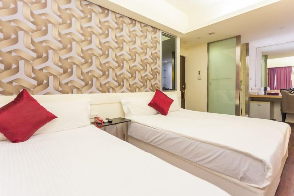 A hotel room with two beds, a desk, and a mirror.