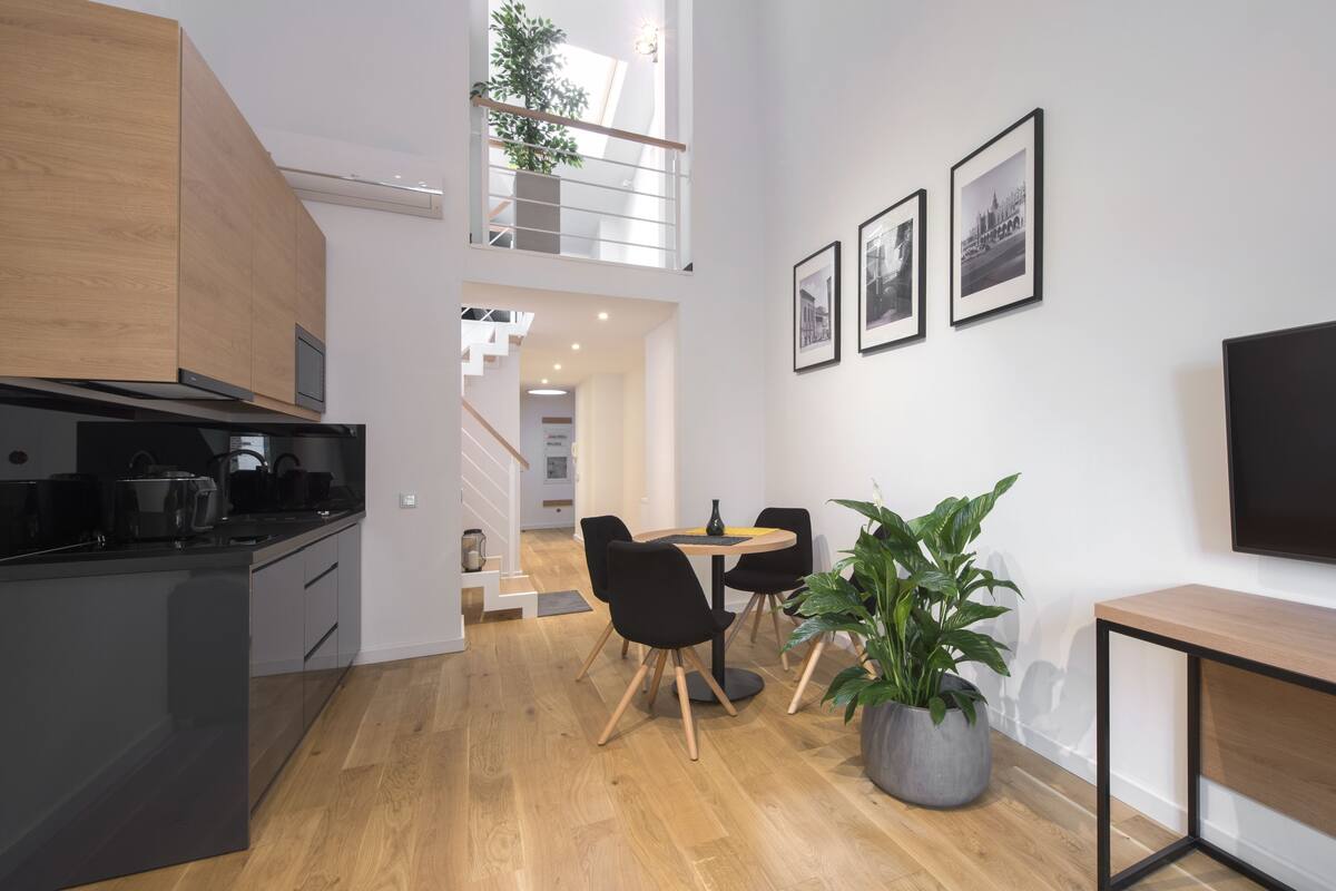 A modern kitchen with a dining area, wooden flooring, and a staircase leading to an upper level.