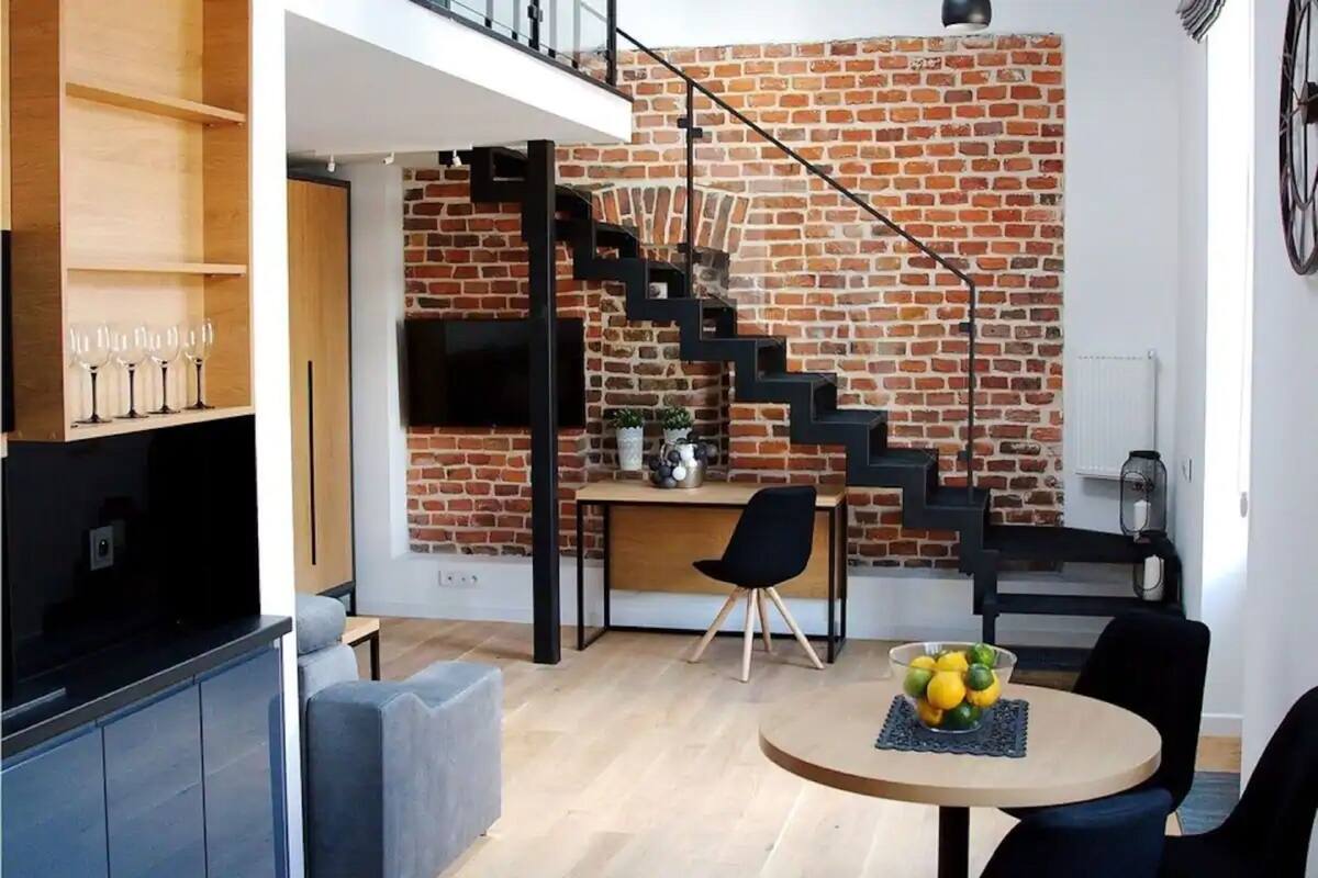 A modern living space with a brick wall, a staircase, a dining area with a round table, and a sofa.
