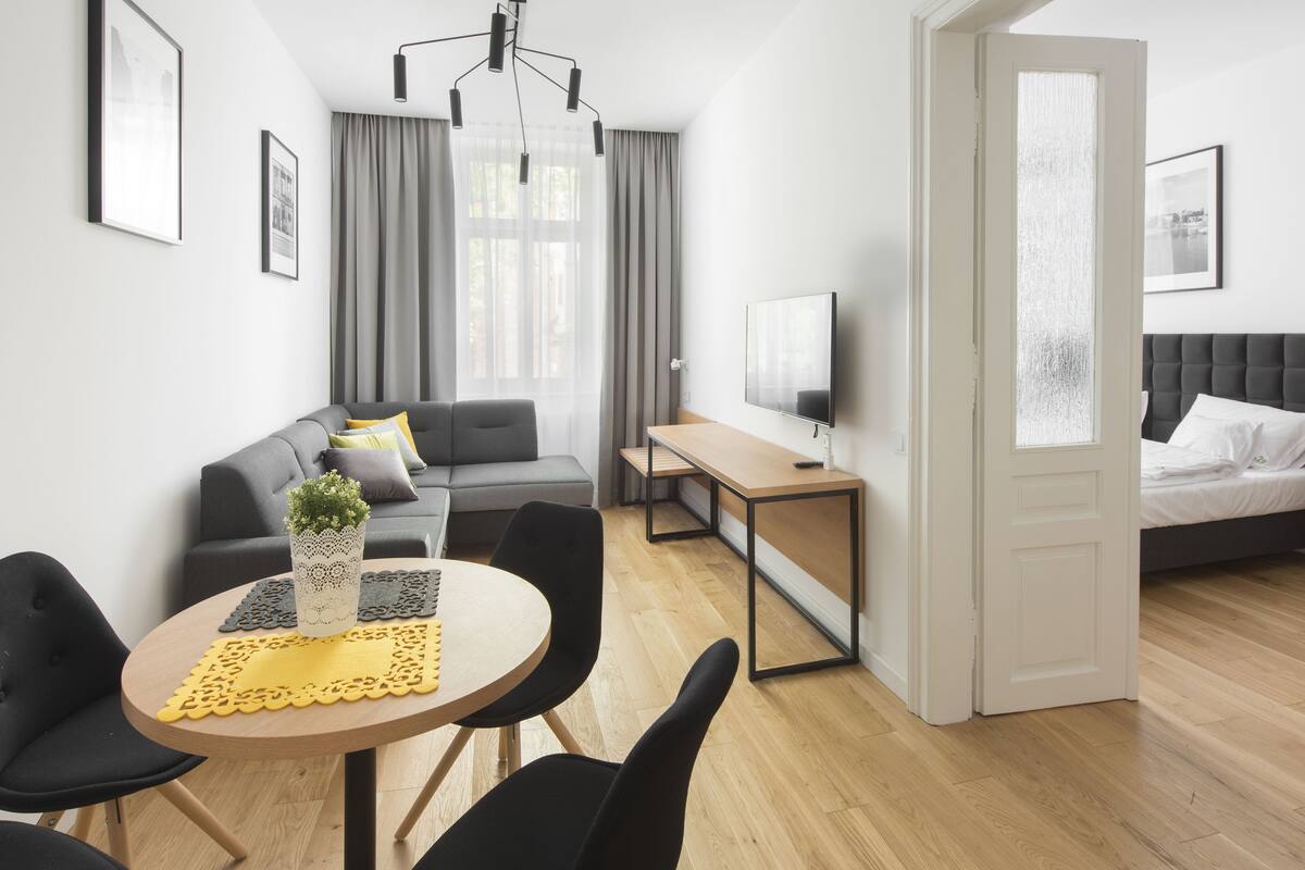 A modern living room with a sofa, a dining table with chairs, a TV, and a bed.