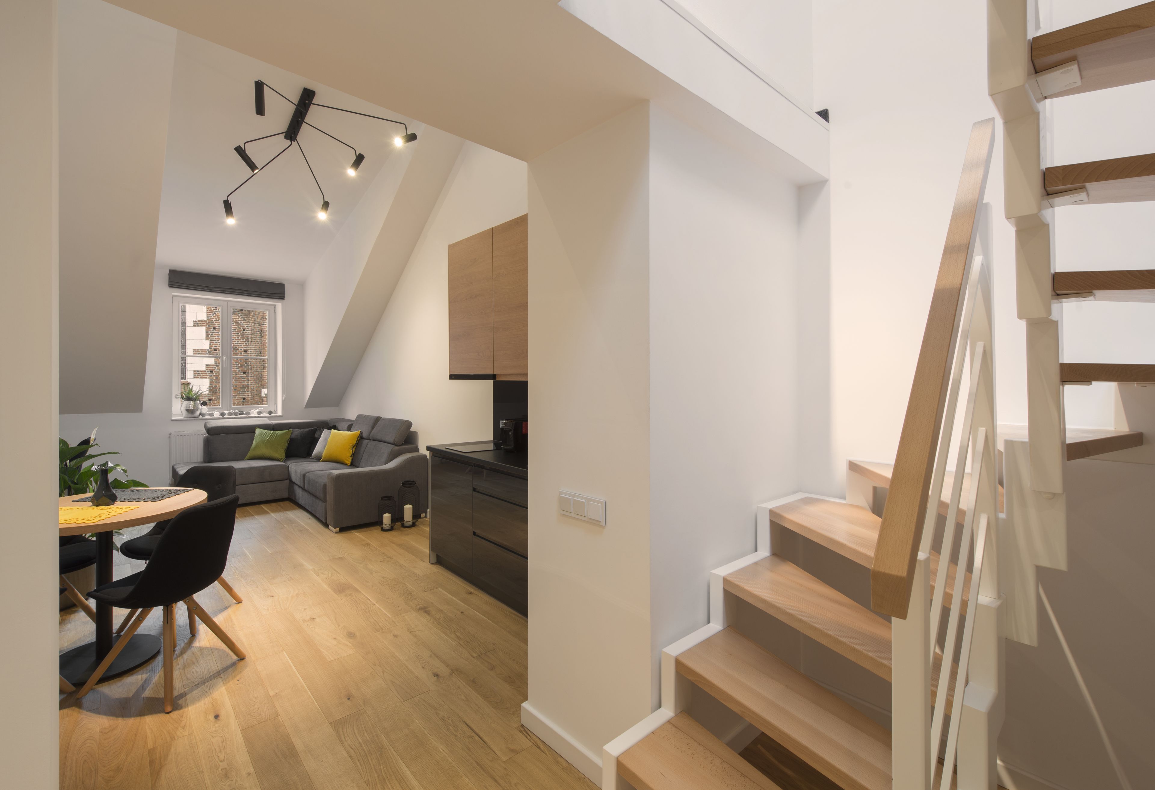 A modern interior with a dining area, a gray sofa, and a staircase.
