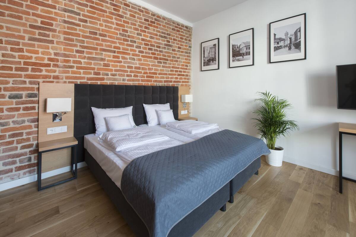 A modern bedroom with a brick wall, a large bed, bedside tables, a TV, and framed pictures on the wall.