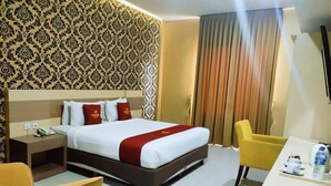A hotel room with a large bed, a bedside table with a phone, a yellow chair, and a desk with a water bottle. - Grand Dian Boutique Hotel (North Cirebon)