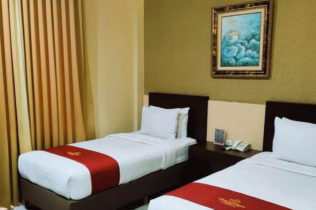 A hotel room with two beds, beige curtains, a painting on the wall, and a phone on the nightstand.