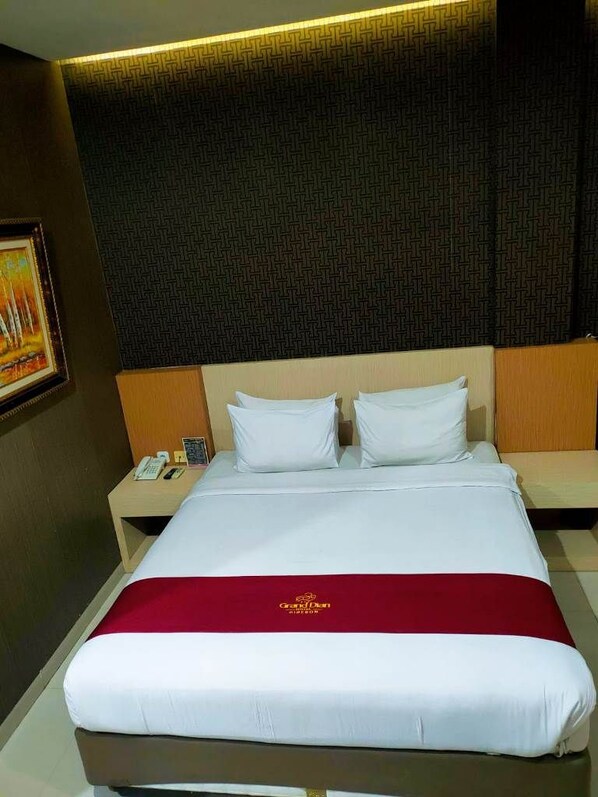 A hotel room with a large bed, a bedside table with a phone and a book, and a red bedspread.