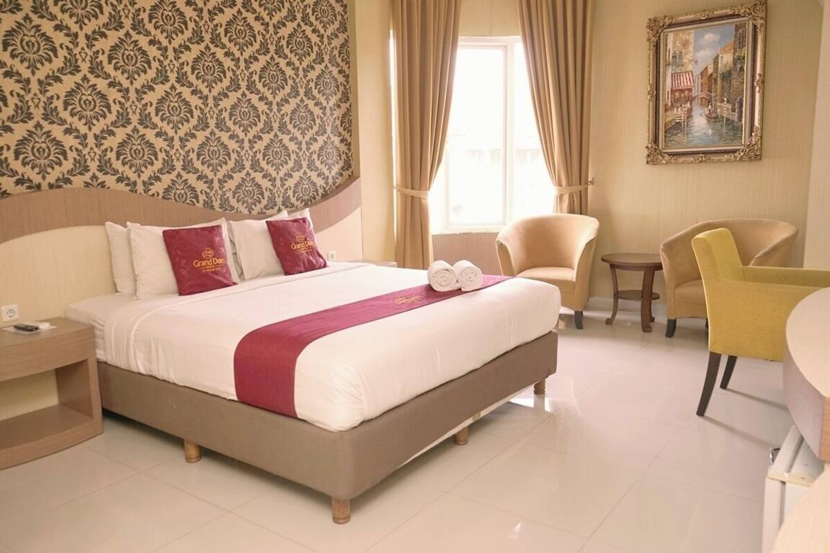 A hotel room with a large bed, a small table, two chairs, and a painting on the wall.