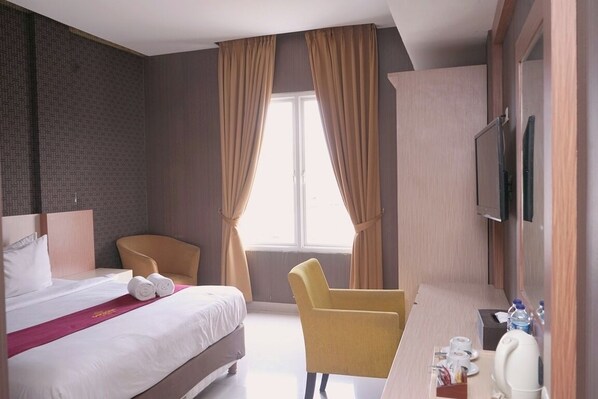 A hotel room with a bed, a chair, a desk, a television, and a window with curtains.