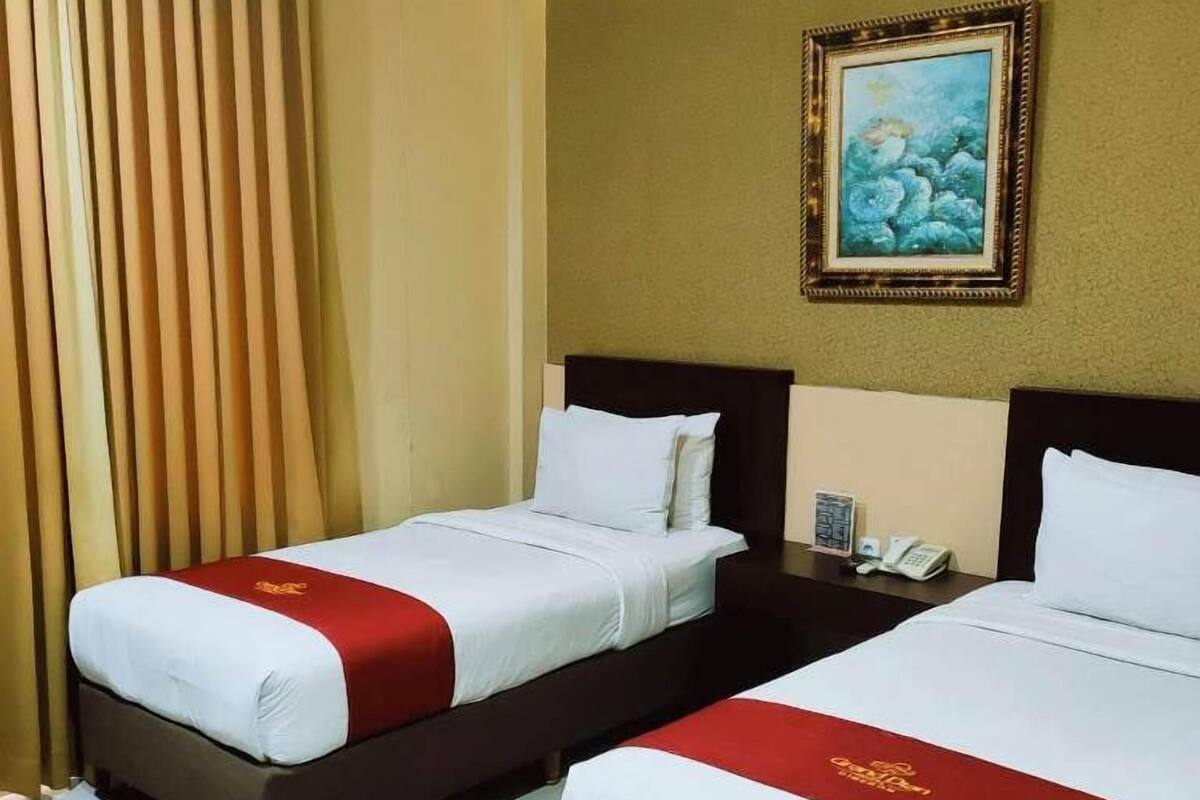 A hotel room with two beds, a painting on the wall, and a telephone on the nightstand.