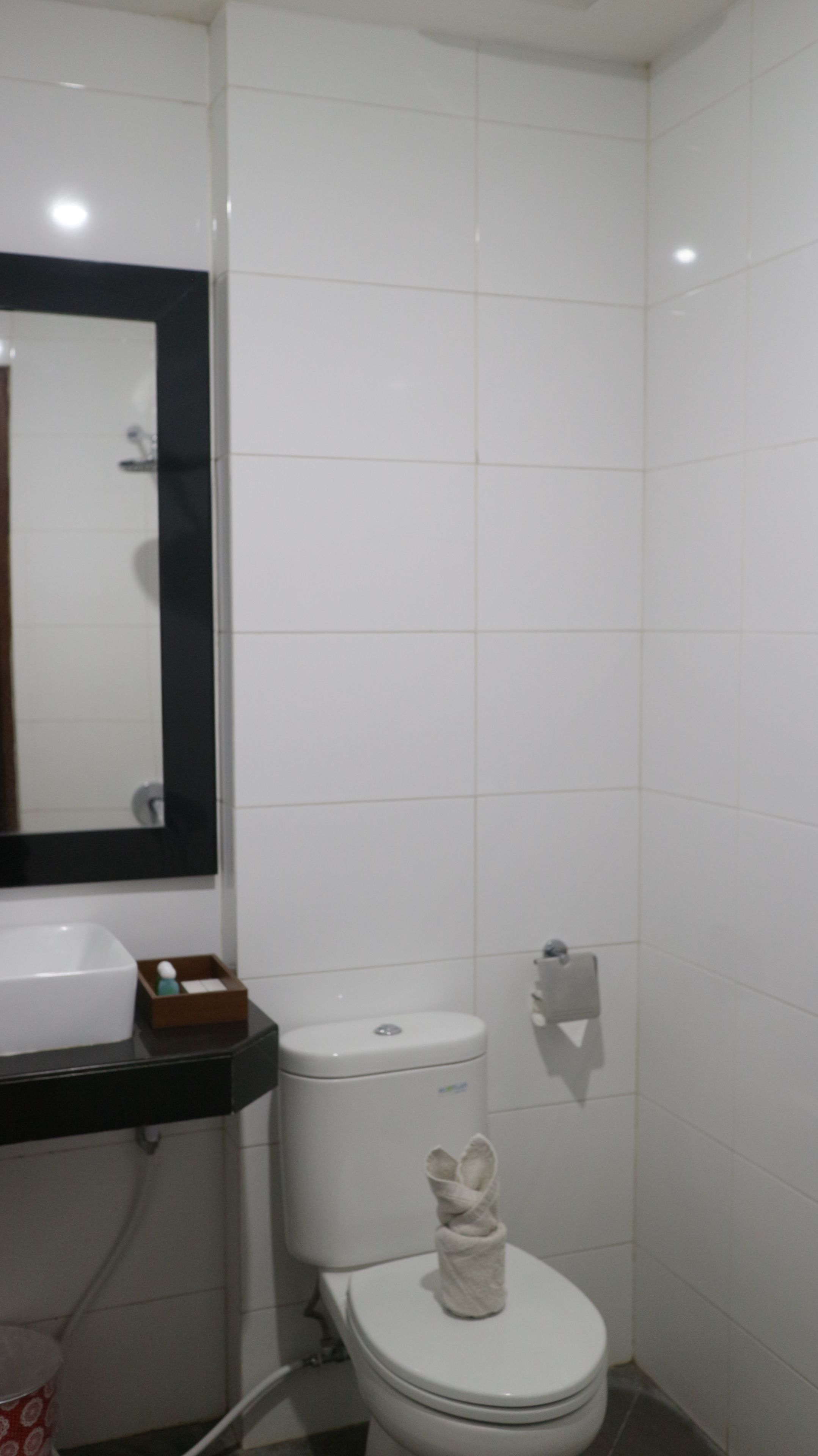 Un baño pequeño y limpio con azulejos blancos, un inodoro, un lavamanos y un espejo.