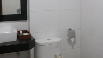 Un baño pequeño y limpio con azulejos blancos, un inodoro, un lavamanos y un espejo.