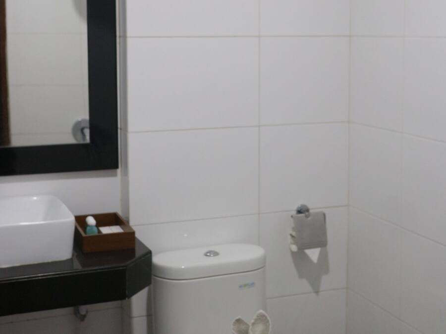 Un baño pequeño y limpio con azulejos blancos, un inodoro, un lavamanos y un espejo.