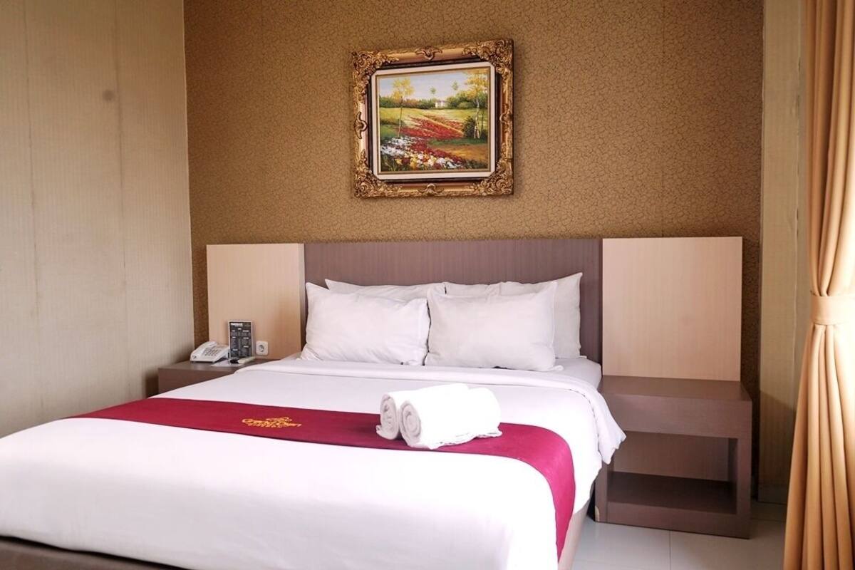A hotel room with a large bed, a nightstand with a phone, and a painting on the wall.