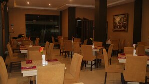 A restaurant with multiple tables and chairs, a painting on the wall, and a large window in the background. - Grand Dian Boutique Hotel (North Cirebon)