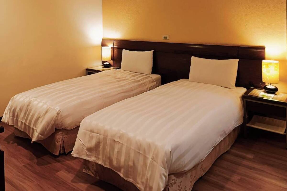 A hotel room with two single beds, wooden flooring, and a ceiling light.