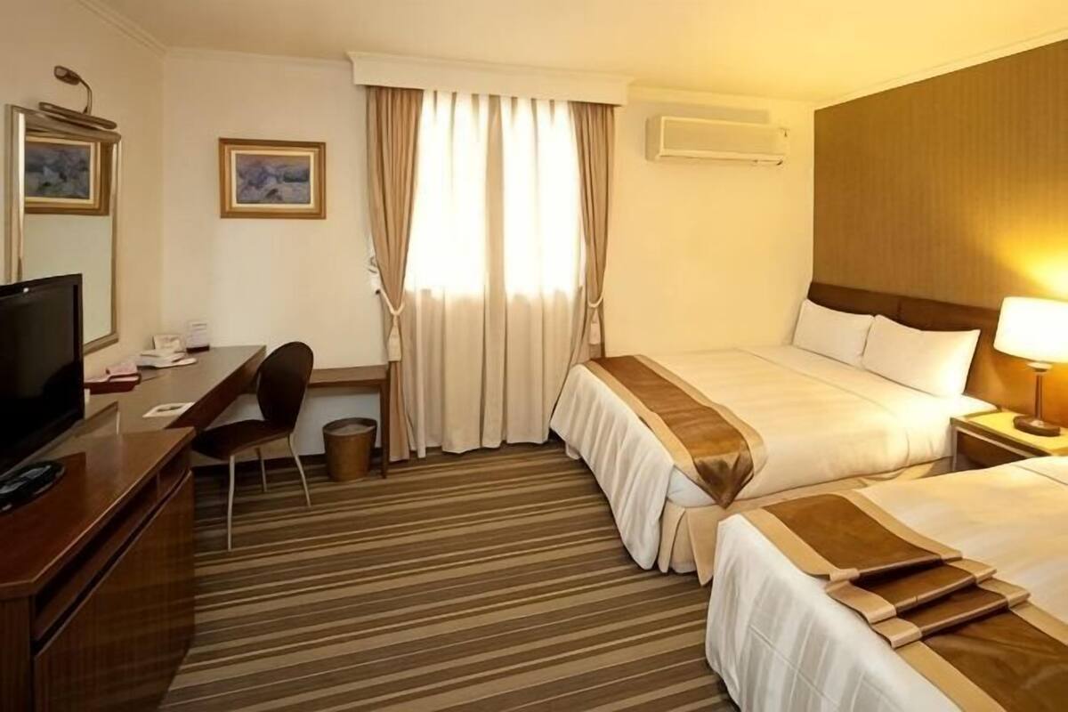A hotel room with a bed, desk, chair, television, and a window with curtains.