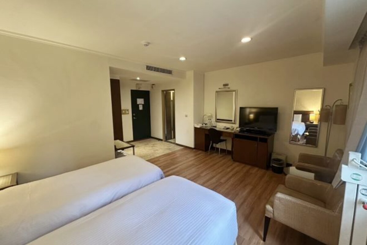 A hotel room with two beds, a desk with a computer, a television, and a mirror.