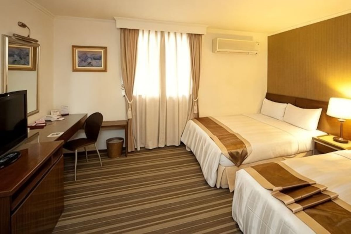 A hotel room with a bed, desk, chair, television, and a window with curtains.