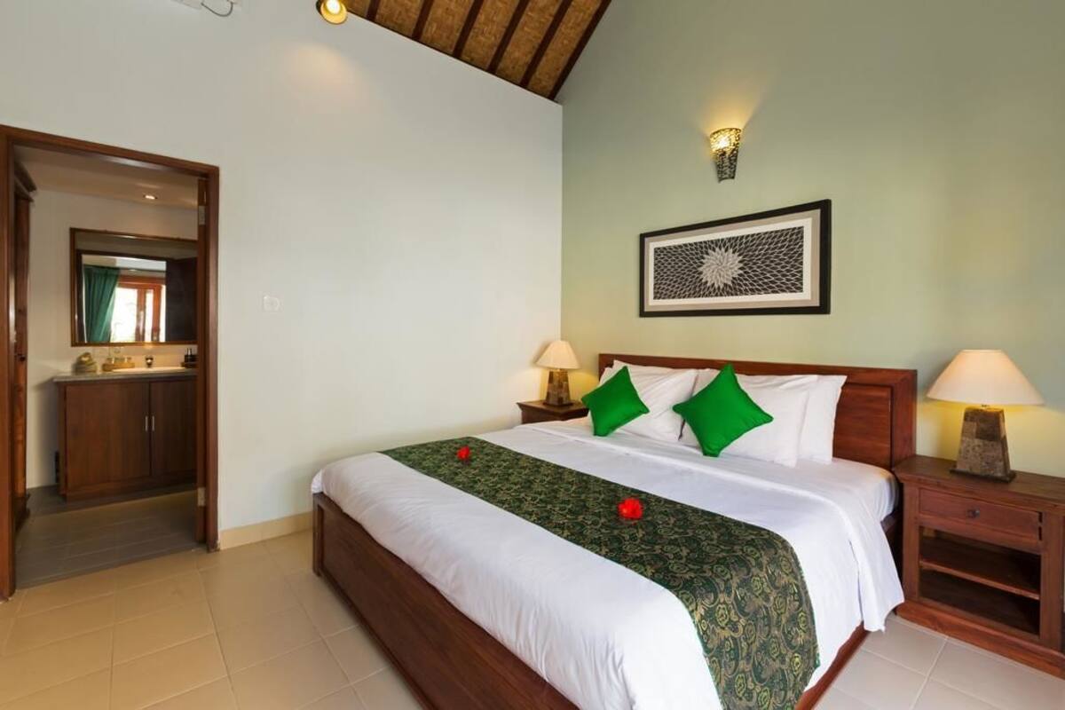 A neatly arranged hotel room with a large bed, two bedside tables with lamps, a framed artwork on the wall, and a wooden wardrobe.